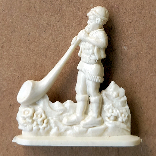 Vintage margarine figurine of an alphorn player in traditional folklore costume holding a long alpine horn