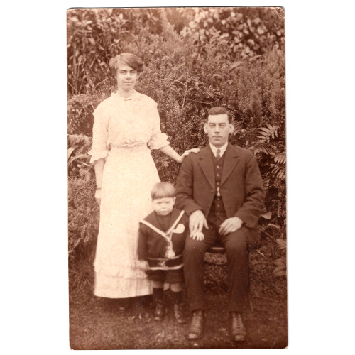 Vintage family postcard showing a seated man, woman dressed in white, and child posing for a studio portrait.