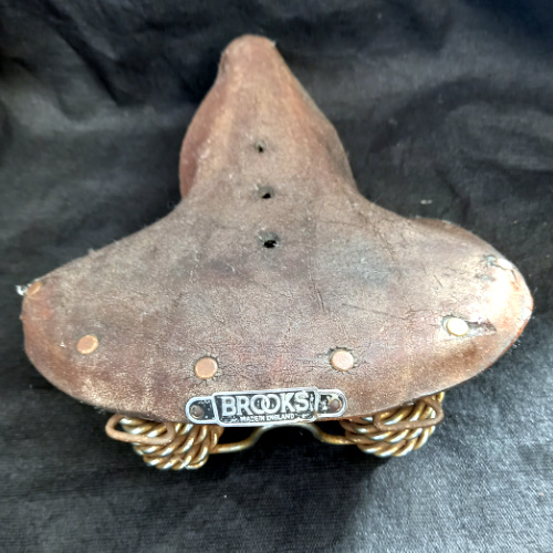 Well-worn vintage Brooks B33 leather bicycle saddle made in England with original sprung steel frame.