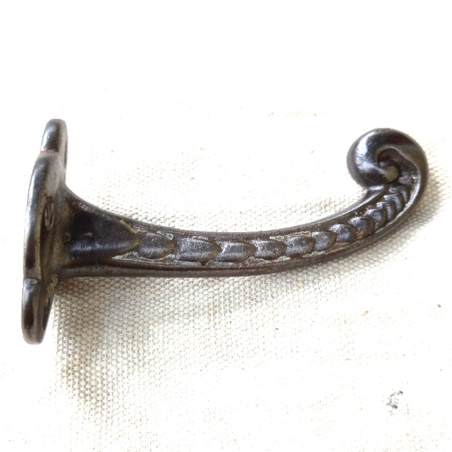 Vintage cast iron wall hook with curled tip and raised decorative detailing