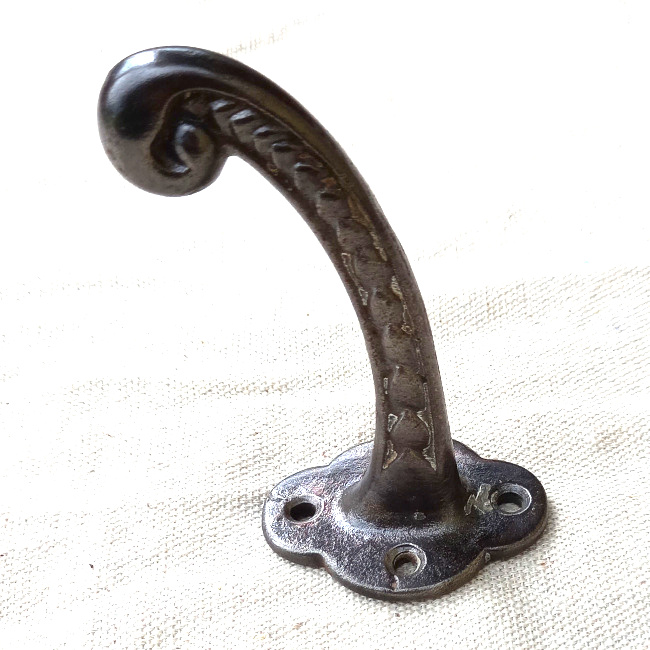 Vintage cast iron wall hook with curled tip and raised decorative detailing
