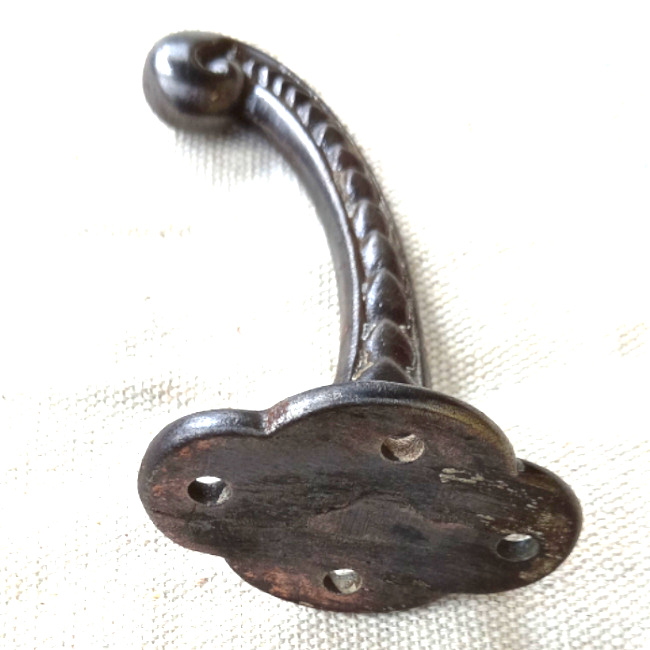 Vintage cast iron wall hook with curled tip and raised decorative detailing