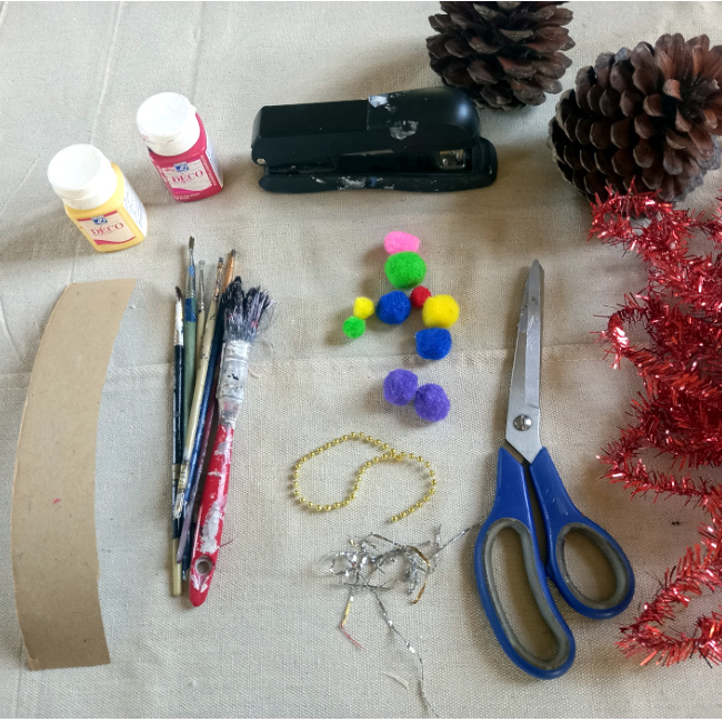 Handmade pine cone Christmas tree decorated with paint, glitter, tinsel and colourful beads on a festive base