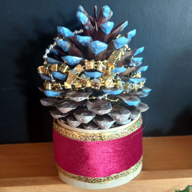 Handmade pine cone Christmas tree decorated with paint, glitter, tinsel and colourful beads on a festive base
