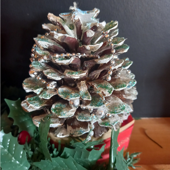 Handmade pine cone Christmas tree decorated with paint, glitter, tinsel and colourful beads on a festive base