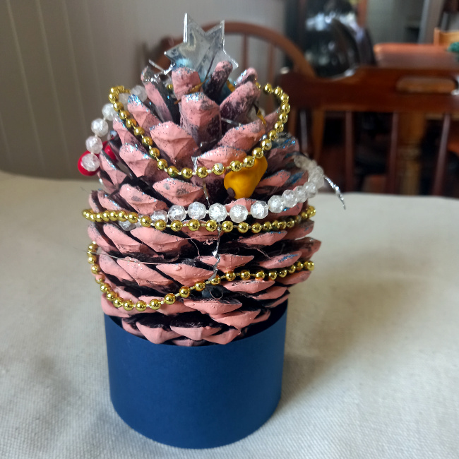 Handmade pine cone Christmas tree decorated with paint, glitter, tinsel and colourful beads on a festive base