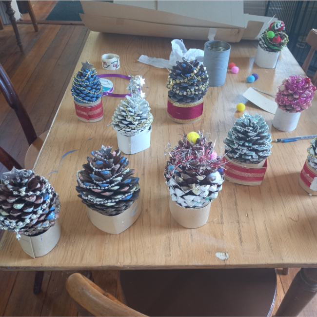 Handmade pine cone Christmas tree decorated with paint, glitter, tinsel and colourful beads on a festive base