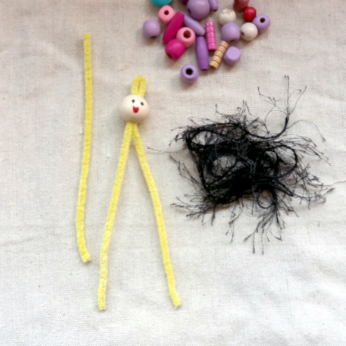 Handmade pipe cleaner person with a beaded body, wool hair and a painted bead face